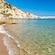 A sandy beach with clear water gently lapping the shore, surrounded by rocky cliffs